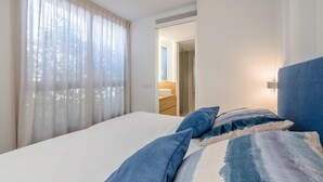A bedroom with a bed, curtains, and a view of a bathroom. - X-3 Ground floor apartment in community with pool (Calella de Palafrugell)