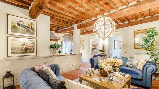 Amplia sala de estar con techo de madera alto, un sofá azul, una mesa de centro de madera con revistas y un candelabro de cristal colgante.