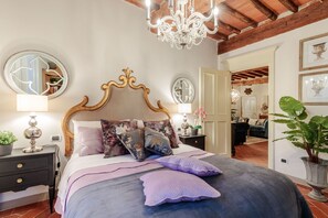 A bedroom with a large bed, ornate headboard, two bedside tables, a chandelier, and a mirror. - CASA KATHY: Smart and Convenient Luxury 2 Bedrooms Apartment inside the City Walls (Lucca)