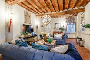 A living room with a blue sofa, a wooden ceiling, a TV, and a fireplace. - CASA KATHY: Smart and Convenient Luxury 2 Bedrooms Apartment inside the City Walls (Lucca)