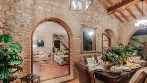 A rustic dining area with brick walls, wooden beams, and a mix of seating including a table set for a meal and wicker chairs.