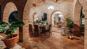 An indoor patio with brick arches, a dining area with wicker chairs, and potted plants.