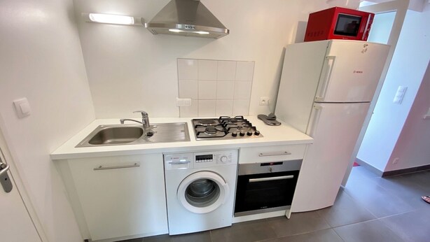 Une cuisine compacte équipée d’un évier, d’une cuisinière, d’un four à micro-ondes et d’un lave-linge.