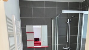 Une salle de bain moderne avec une douche à parois de verre, un lavabo sur colonne et un miroir à cadre rouge.