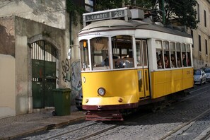 Een gele tram met passagiers, geparkeerd op een kinderafsluiting geplaveid straat.