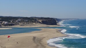 Una playa costera con orilla arenosa, olas y un acantilado al fondo.