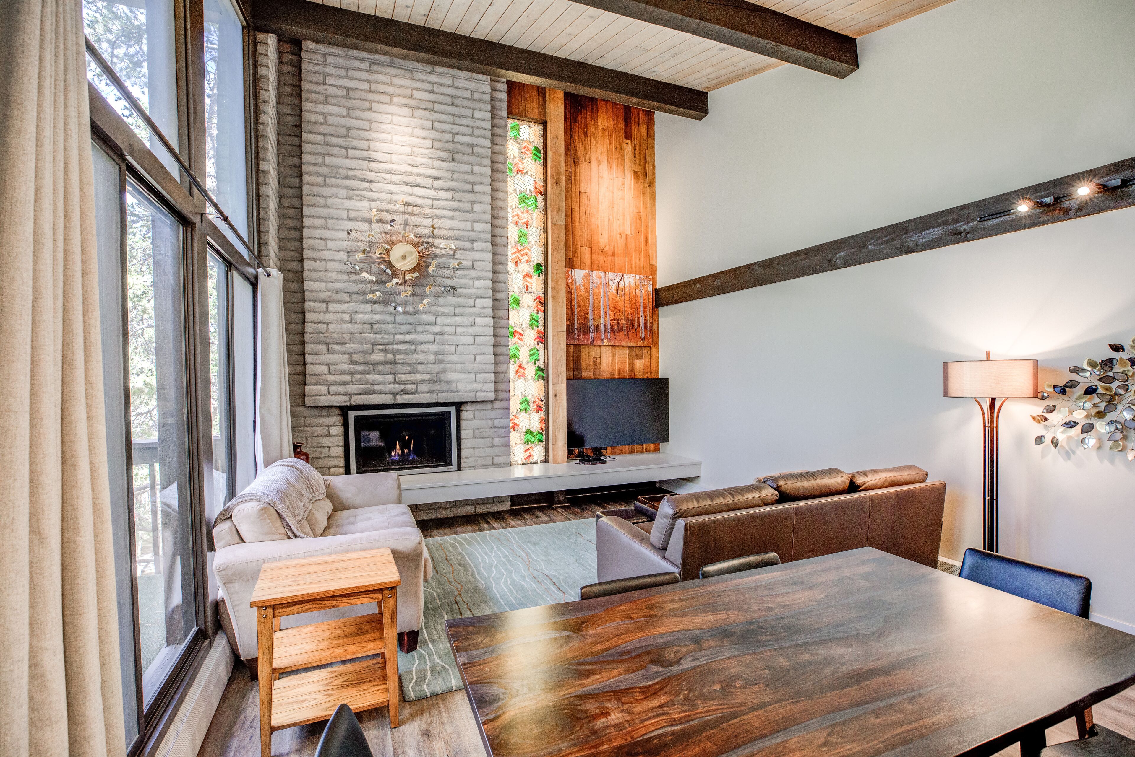 Un salon moderne avec une cheminée, une grande table à manger en bois et un téléviseur fixé au mur.
