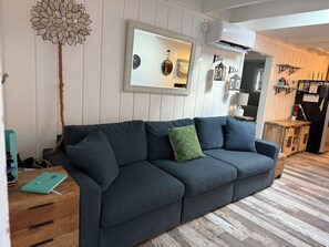 Un salon avec un canapé bleu foncé, une table d’appoint en bois et un miroir au mur.