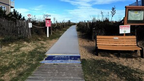 Un sendero que lleva a una playa con un banco de madera y señales de advertencia.
