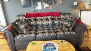 Una sala de estar con un sofá gris, una manta roja y una mesa de centro de madera con revistas y una tarjeta.