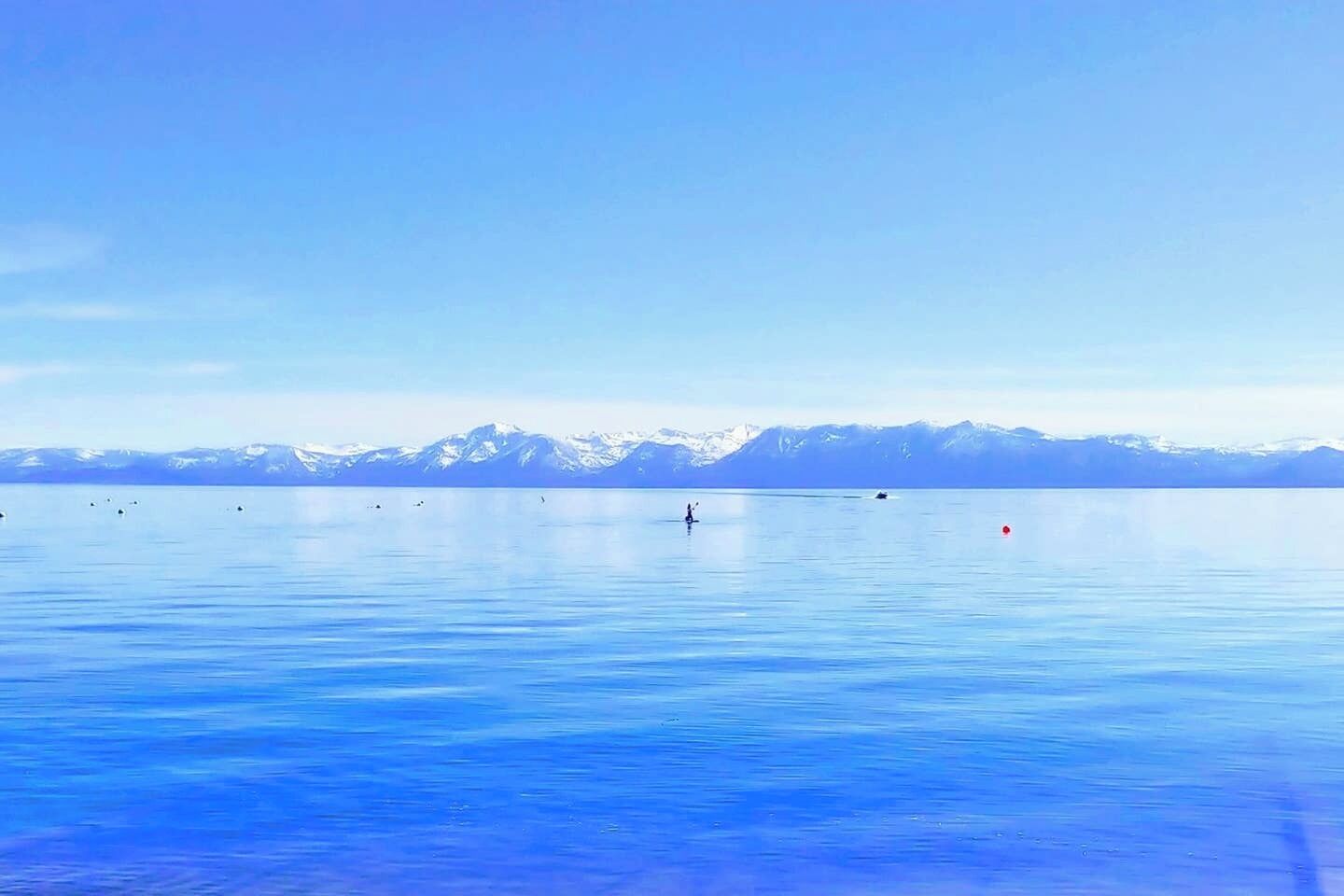 A calm lake with a clear sky and distant snow-capped mountains.