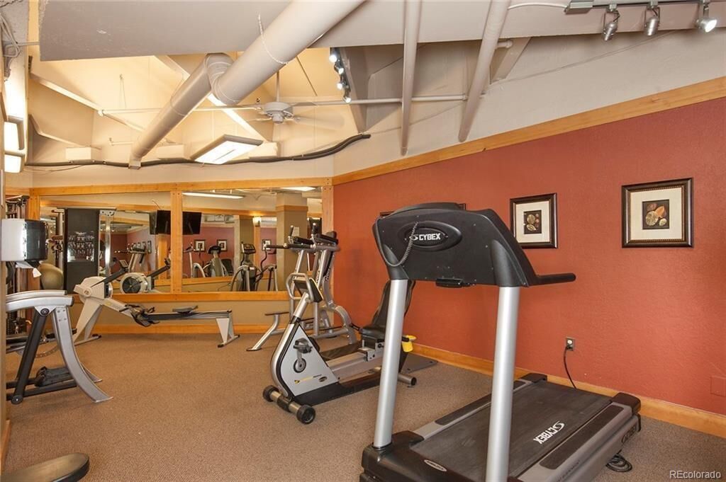 Un gimnasio con equipo cardiovascular, un espejo grande y una pared roja decorada con fotografías enmarcadas.