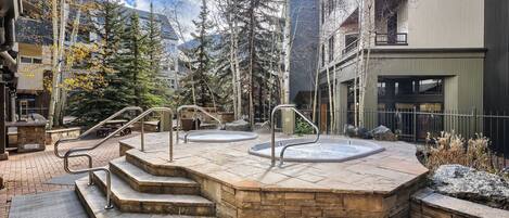 A spa area with stone steps leading to hot tubs, surrounded by trees and modern buildings.