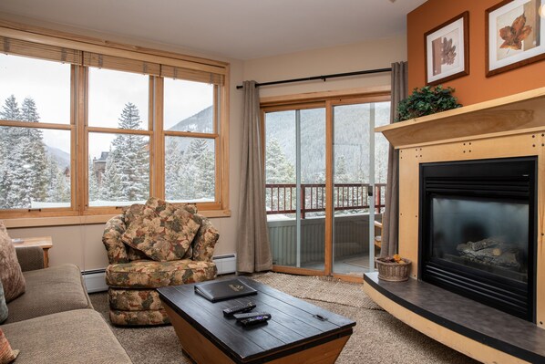 Relax by the fireplace in this inviting living room with a scenic view of snow-covered mountains.