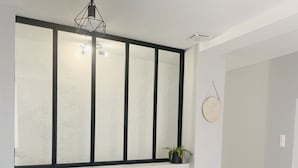 Zona pranzo con tavolo e sedie in legno, un'ampia finestra con cornice nera e un orologio appeso al muro.