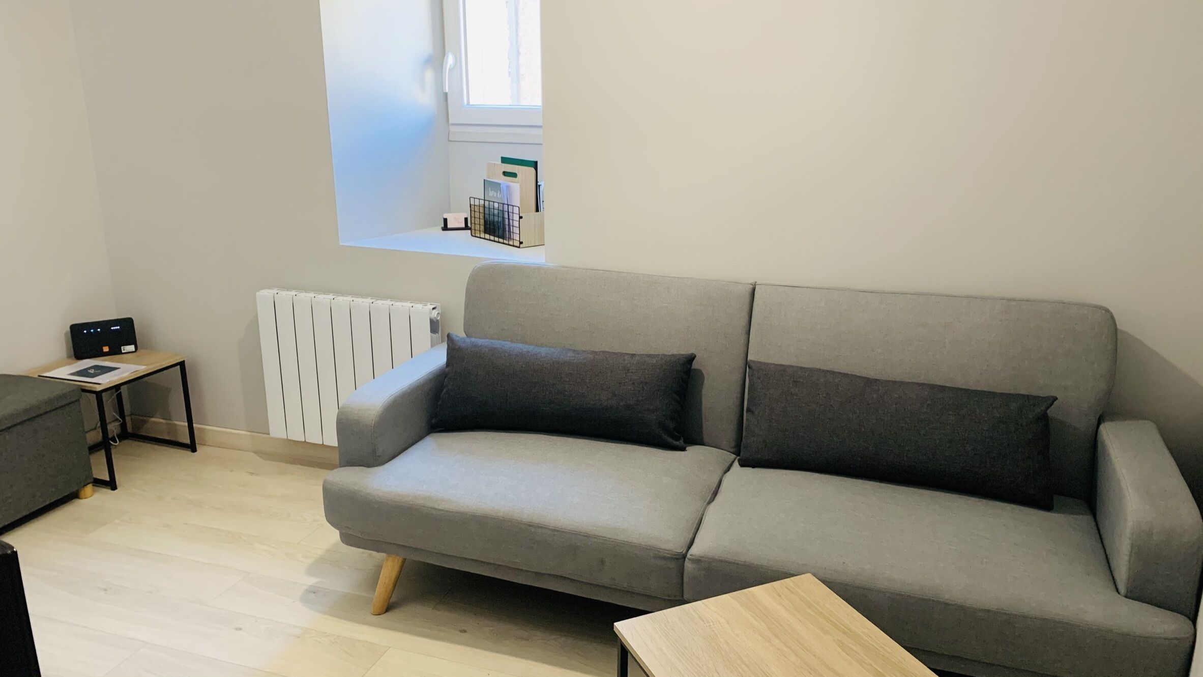 A modern living room with a grey sofa, a small wooden table, and a radiator.