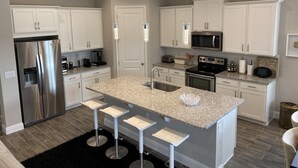 A modern kitchen with white cabinets, stainless steel appliances, a granite countertop, and a central island with bar stools. - Nice designed single family villa facing a lake (Naples)