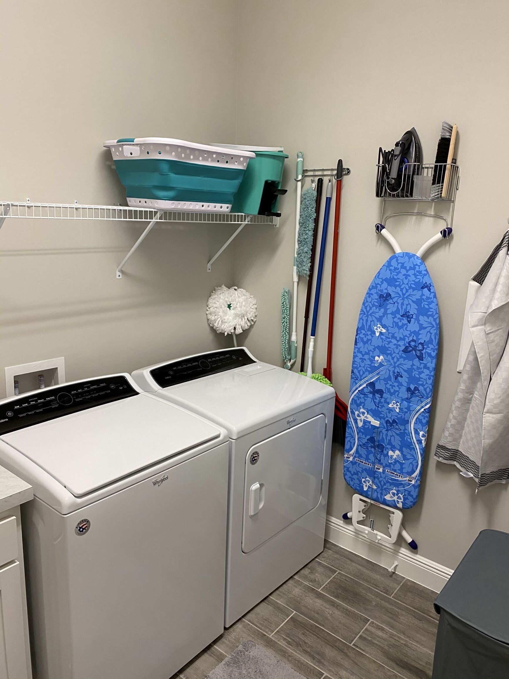 A laundry room with two front-loading washers, a drying rack, and a hanging iron.