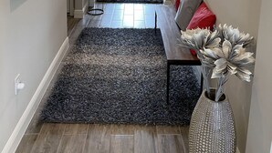 A hallway with a dark rug, a sofa with red cushions, and a vase with artificial flowers. - Nice designed single family villa facing a lake (Naples)