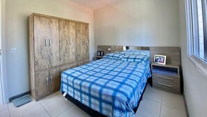 A bedroom with a bed, a wardrobe, a bedside table, and a window. - Pé na Areia (RS)
