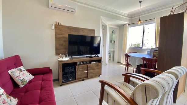 A living room with a red sofa, a TV on a wooden stand, and a dining area with a table and chairs. - Pé na Areia (RS)