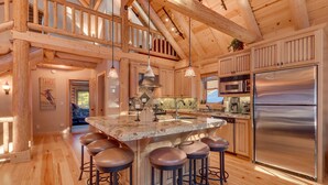 A spacious kitchen with a large island, wooden bar stools, stainless steel appliances, and a high ceiling with exposed beams.