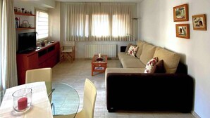 A living room with a sofa, a dining table with chairs, a TV, and a ceiling light. - La Terrassa del Barri Vell de Girona (Girona)