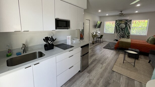 Una cocina moderna con armarios blancos, un lavamanos de acero inoxidable y un microondas integrado.