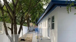 A single-story building with a white exterior and blue trim. There is a covered walkway leading to the entrance, flanked by trees and a white fence. - 526 · Beautiful and Spacious studio - Casa Habana (Little Habana)