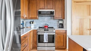 A kitchen with wooden cabinets, stainless steel appliances, and a tiled backsplash. - Dragonfly at the Homestead (Glen Arbor)
