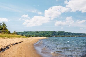 Een strand met een zandstrand, een rustige zee en een beboste heuvel op de achtergrond.