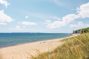 A beach with a clear sky, calm sea, and a distant shoreline. - Dragonfly at the Homestead (Glen Arbor)