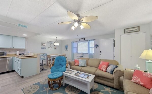 A compact living space with a kitchenette, a blue armchair, a beige sofa, and a ceiling fan. - Oceanside 2bed 2bath condo, close to beach & perfect for families! (Ocean City)