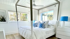 Ein Schlafzimmer mit Baldachinbett, Holzboden, Deckenventilator und Blick ins Freie durch Fenster.