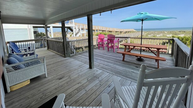 A wooden deck with a view of the ocean, a picnic table, and Adirondack chairs. - Charming oceanfront cottage, pet friendly, private walkway to the beach (Ocean Isle Beach)
