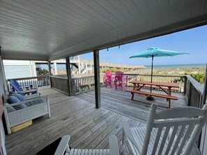 A wooden deck with a view of the ocean, a picnic table, and Adirondack chairs. - Charming oceanfront cottage, pet friendly, private walkway to the beach (Ocean Isle Beach)
