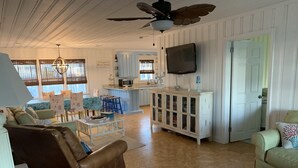 A spacious living room with a brown leather sofa, a white cabinet, and a television mounted on the wall. - Charming oceanfront cottage, pet friendly, private walkway to the beach (Ocean Isle Beach)