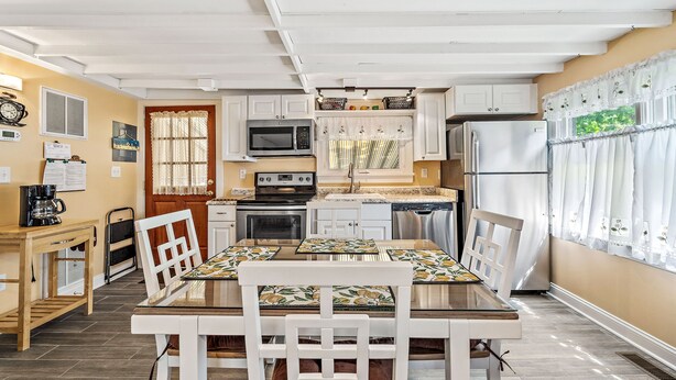A compact kitchen with white cabinets, a microwave, a refrigerator, and a dining area with a table and chairs.