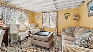 A living room with a patterned armchair, ottoman, and sofa, a coffee table, a lamp, and a wall-mounted welcome sign.