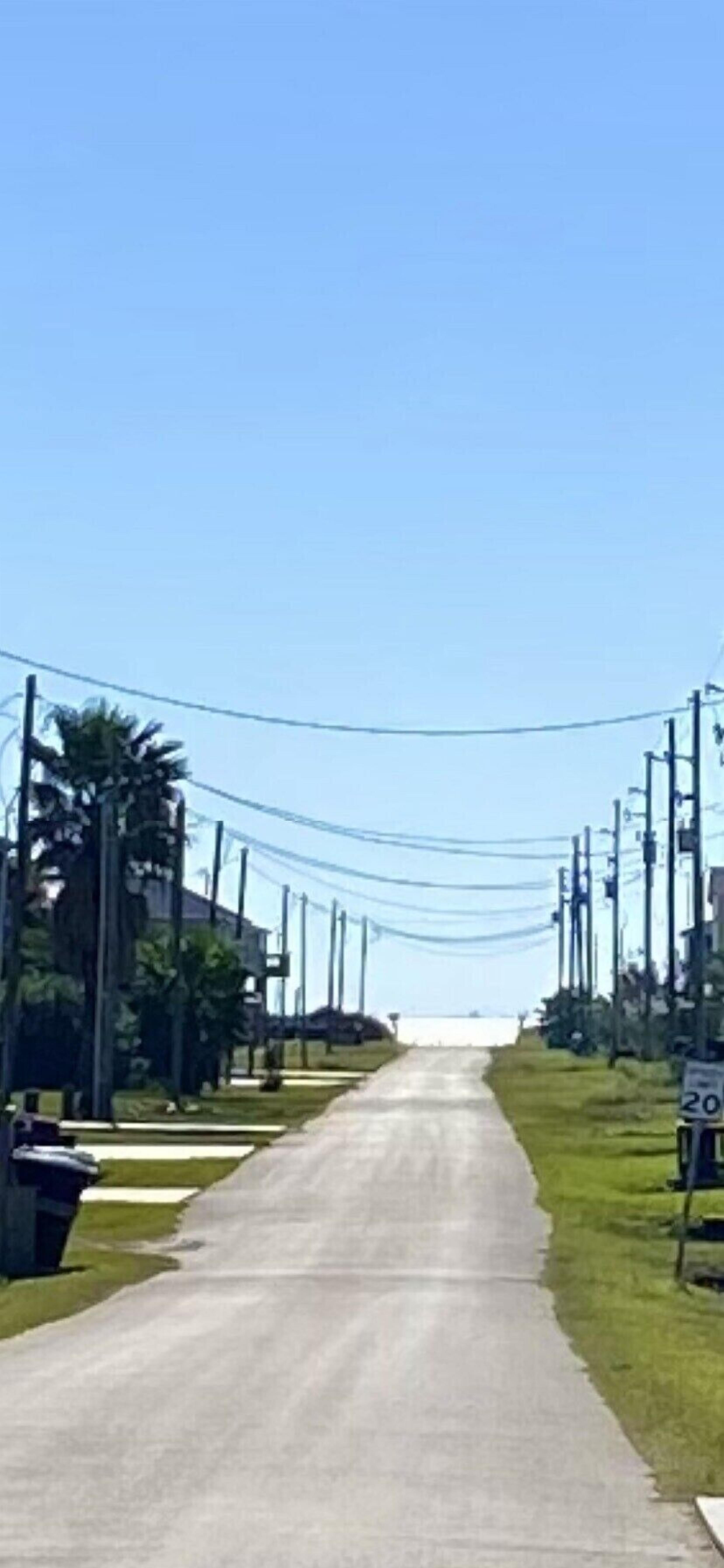 A straight road with a speed limit sign of 20 mph, flanked by utility poles and power lines, leading to a distant horizon.