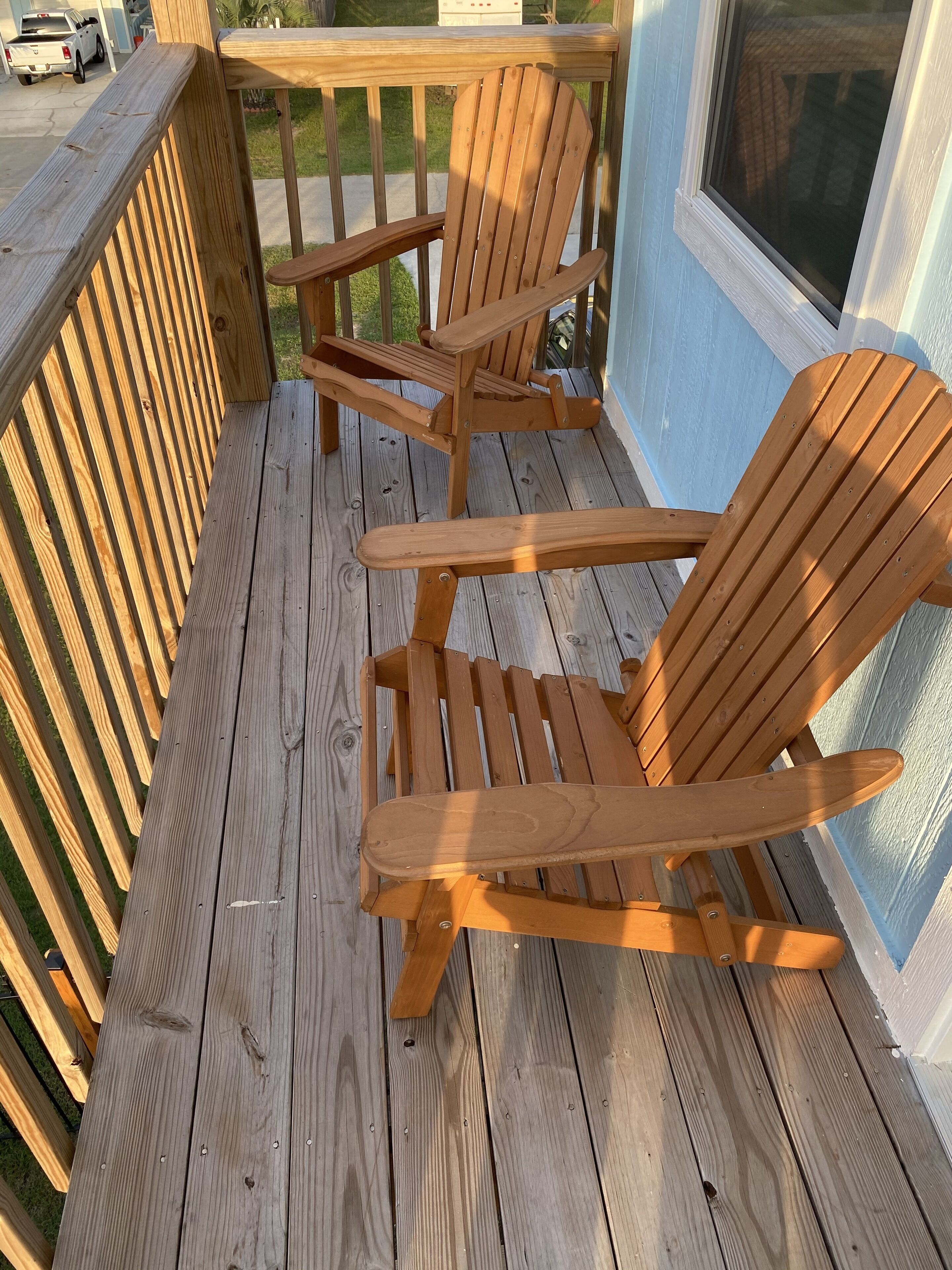 Een houten terras met twee Adirondack-stoelen en een bijzettafeltje.
