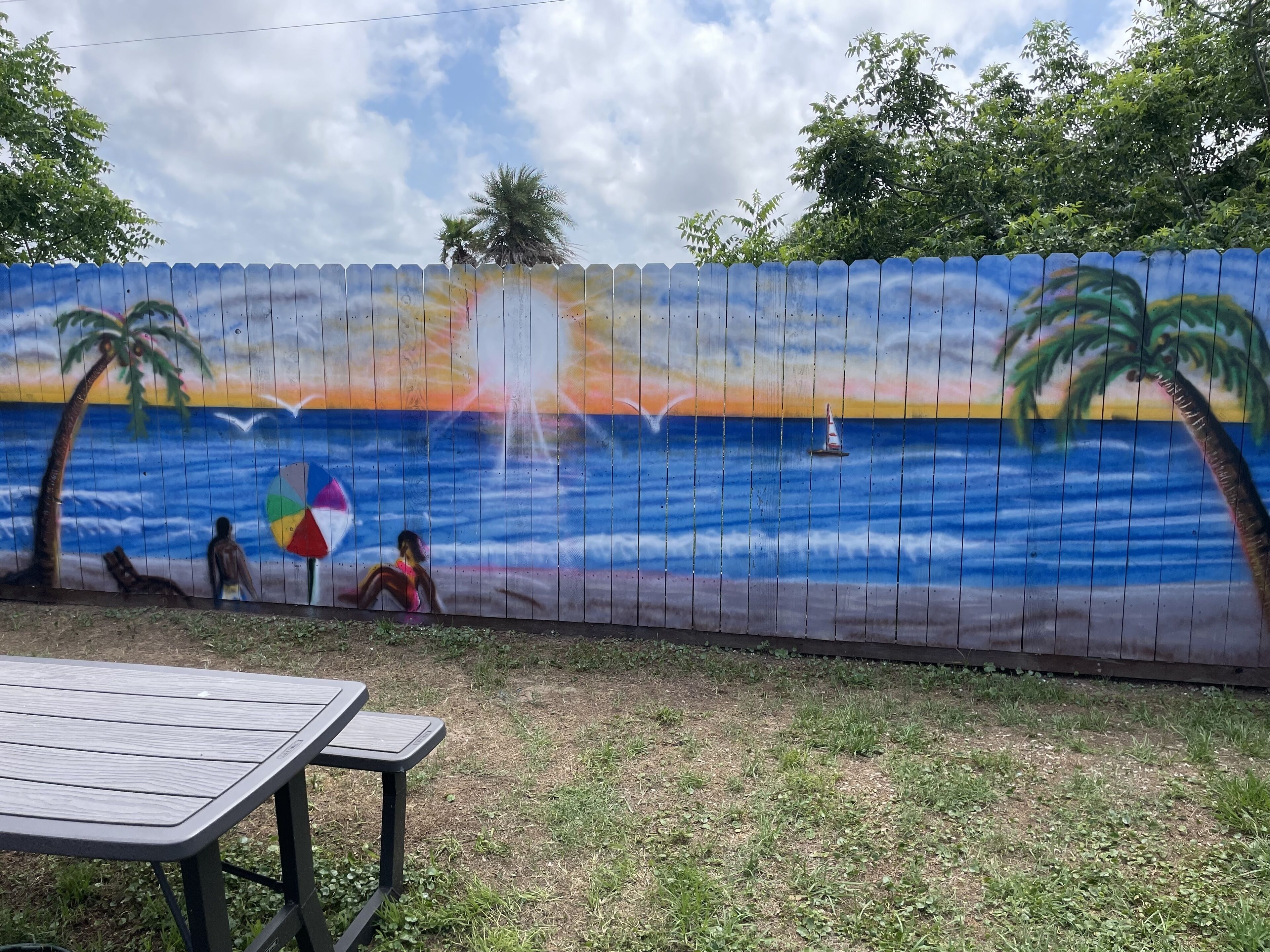 A mural of a sunset over the ocean with palm trees and beachgoers.