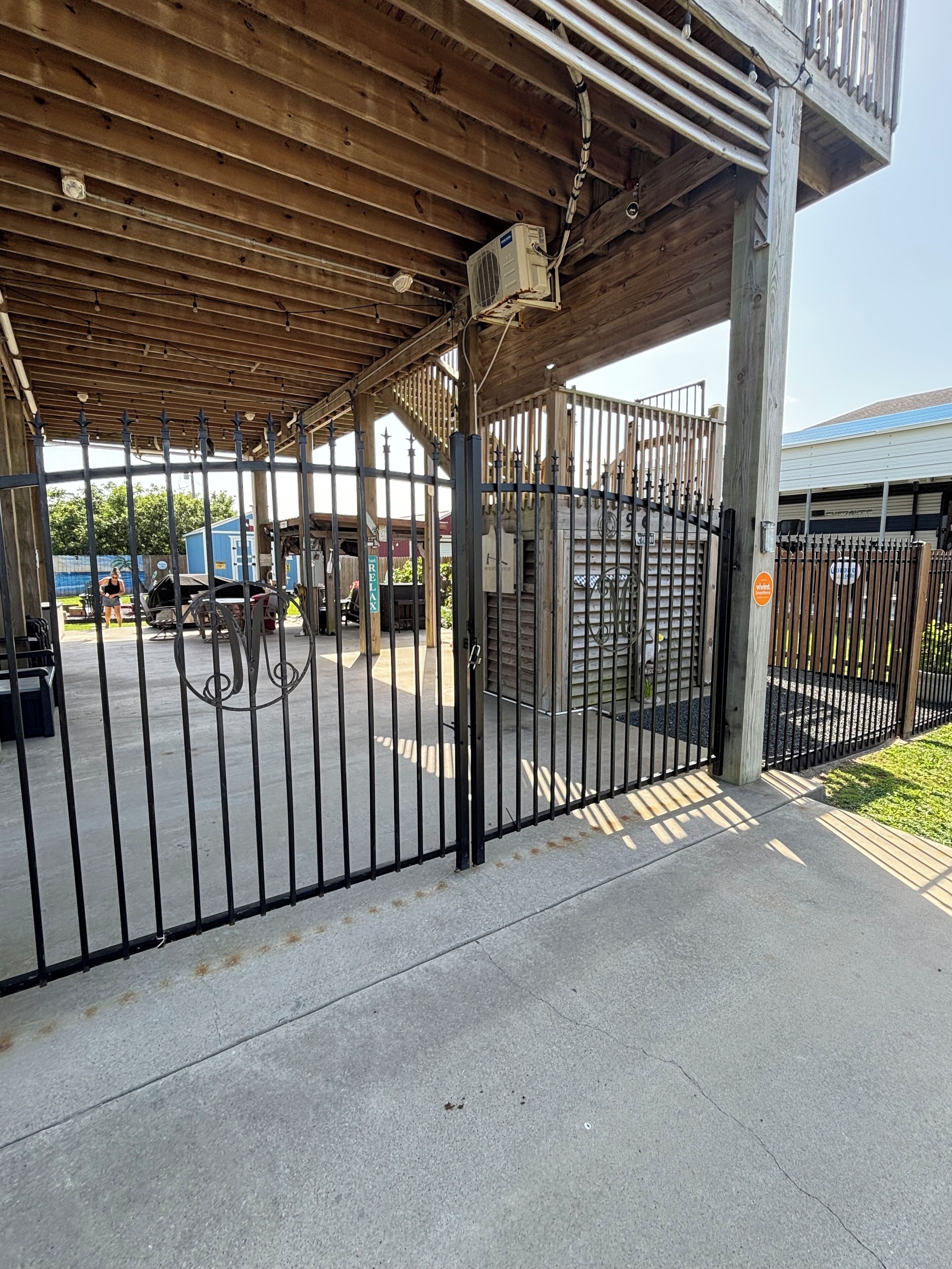 A covered outdoor area with a metal gate, concrete floor, and a wooden structure overhead.
