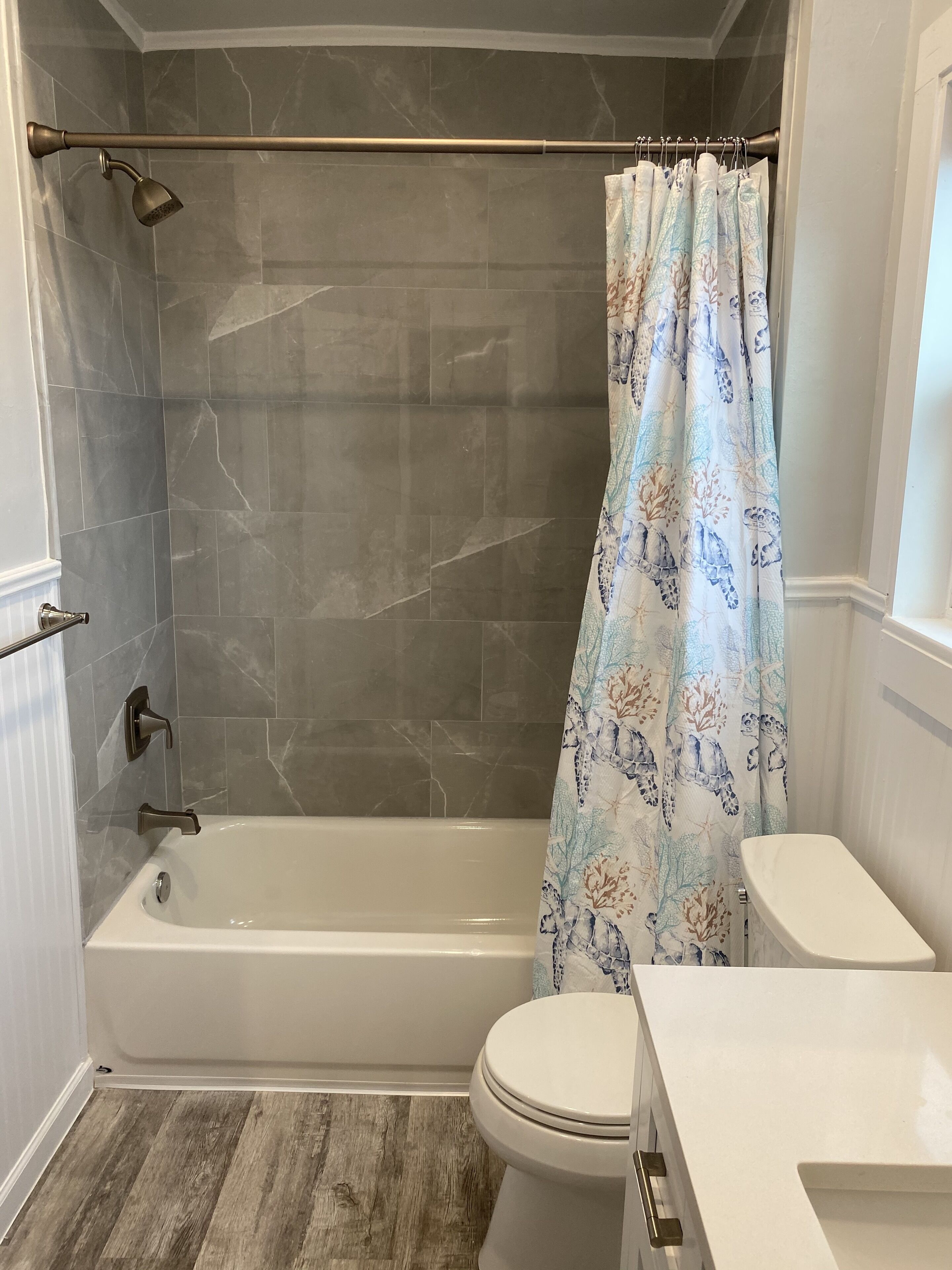 A bathroom with a bathtub, shower, toilet, and a window.