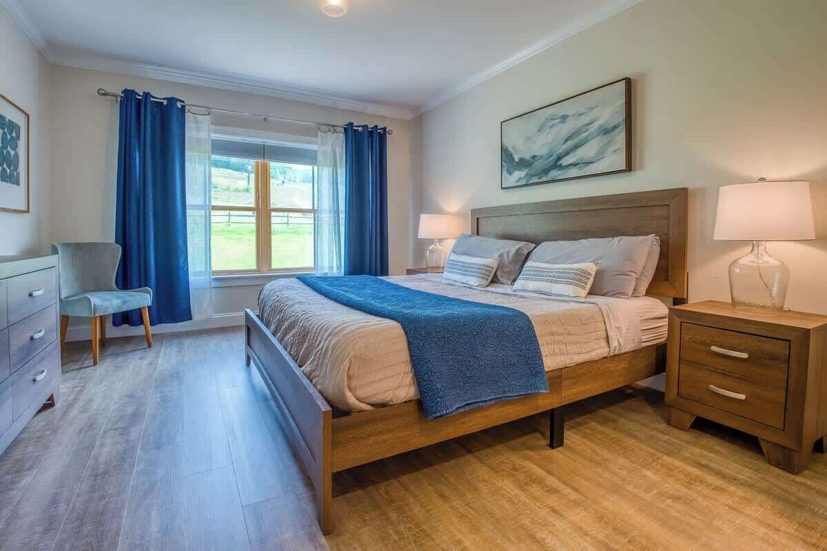 Ein Schlafzimmer mit einem Holzbett, einem Nachttisch, einem Sessel und einem Fenster mit Vorhängen.