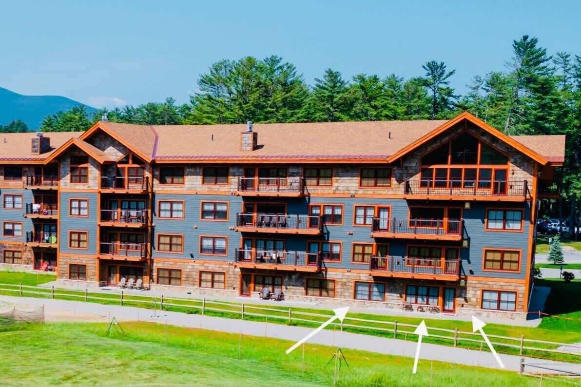 Ein mehrstöckiges Chalet mit Balkonen, einer Steinauffahrt und einer Bergkulisse.