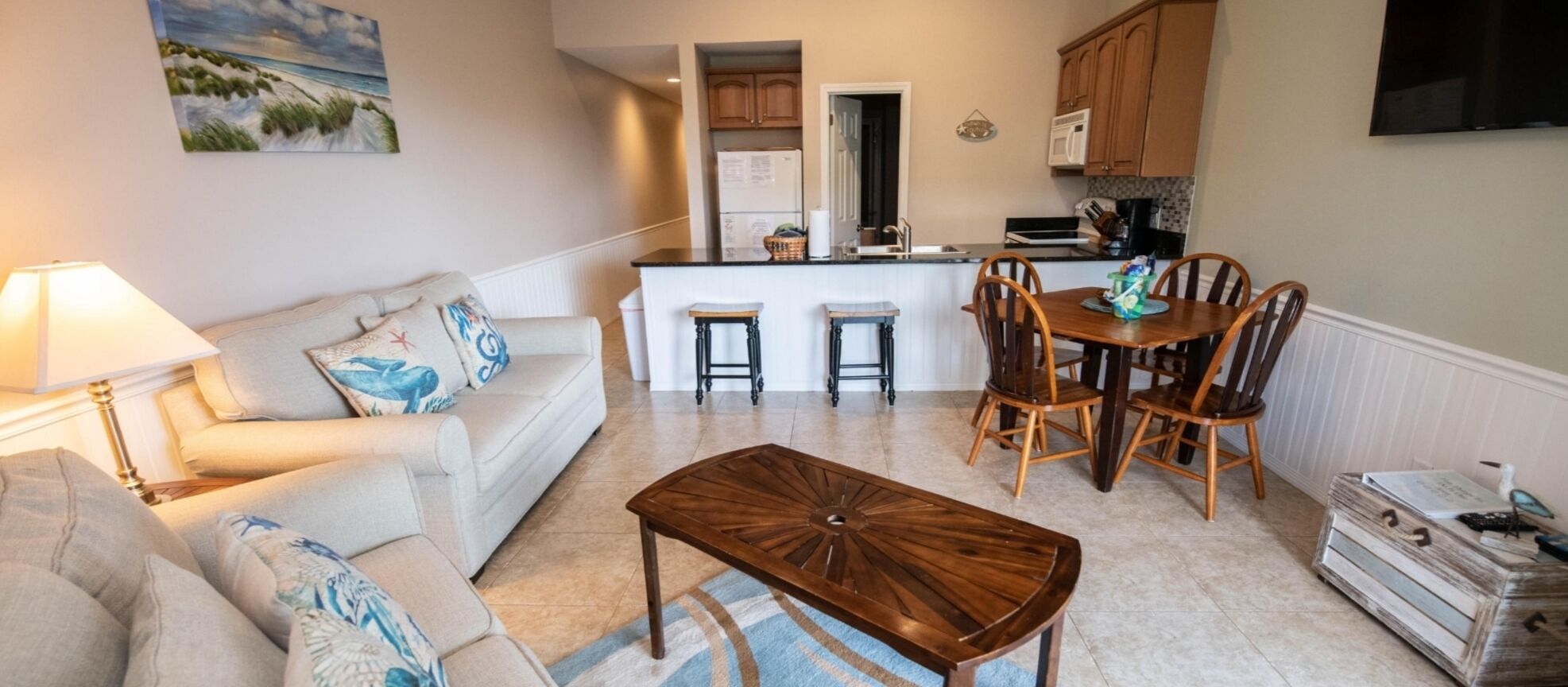 A compact living space with a sofa, a wooden coffee table, a dining area with a table and chairs, and a kitchen area with cabinets and appliances.