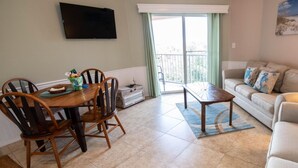 Una sala de estar con sofá, una mesa de centro, una mesa de comedor con sillas, un televisor montado en la pared y vistas al exterior a través de una puerta corrediza.