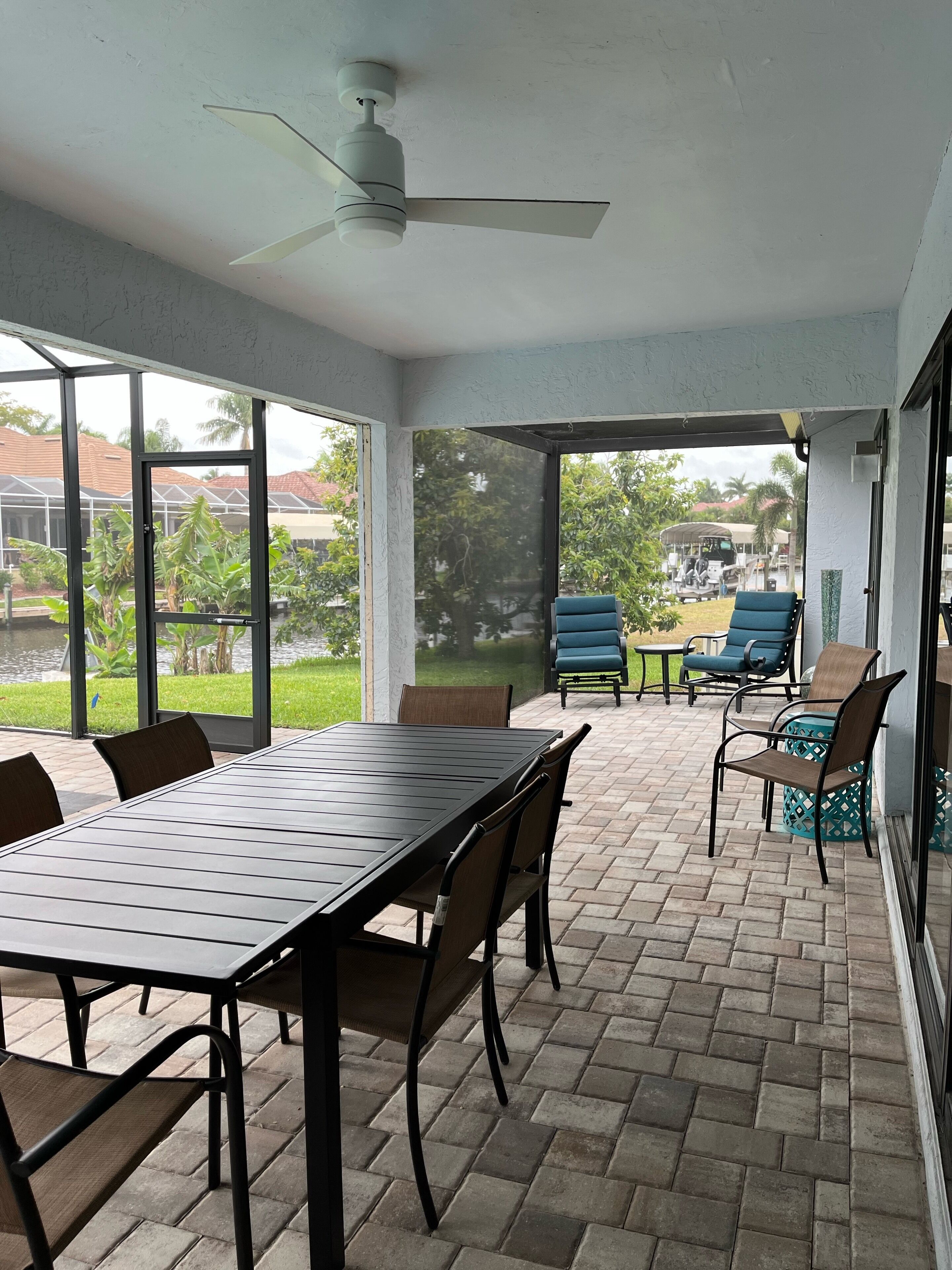 A covered patio area with a table and chairs, large windows, and a ceiling fan.