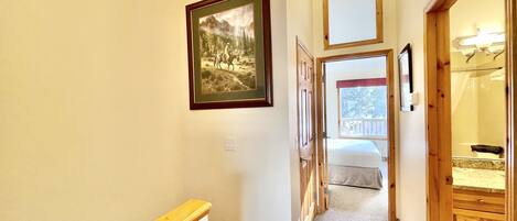 A hallway with a wooden handrail, a framed picture on the wall, and a bed visible through an open door.